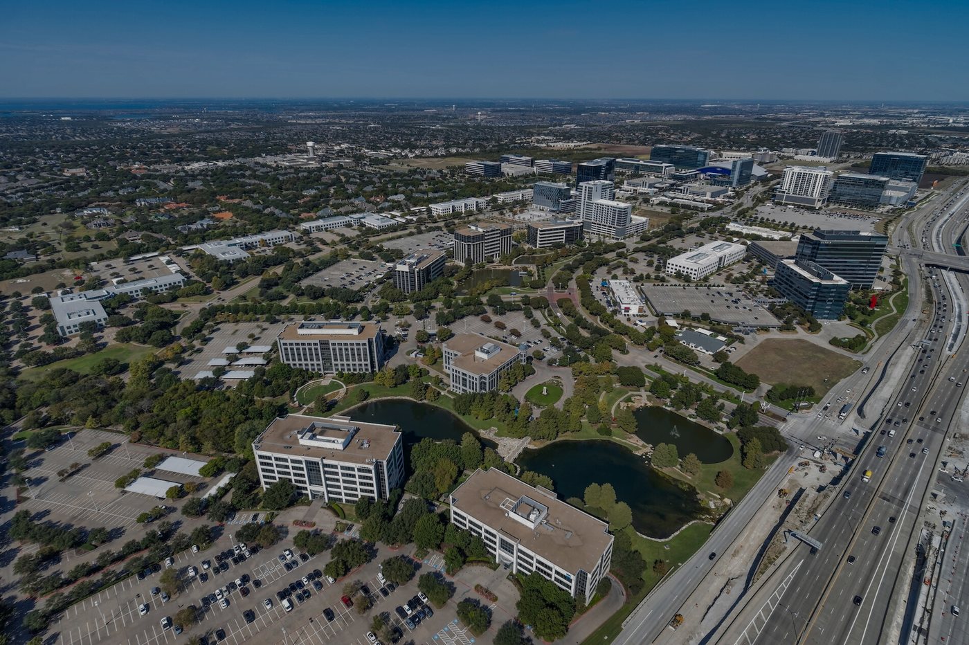 Aerial view of a North Texas corporate office park and freeway corridor under summer sun